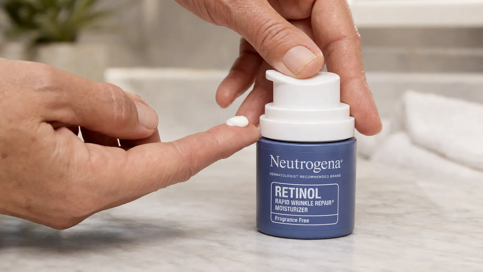 Hand dispensing a pea-sized amount of white retinol face moisturizer from a pump bottle onto a fingertip