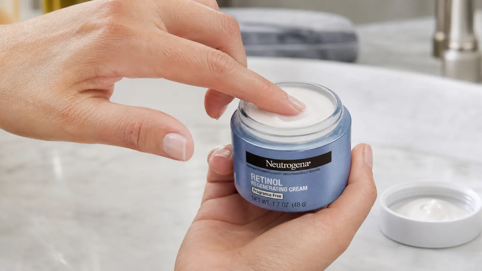 Close-up of a hand scooping a small amount of cream from an open jar with a fingertip